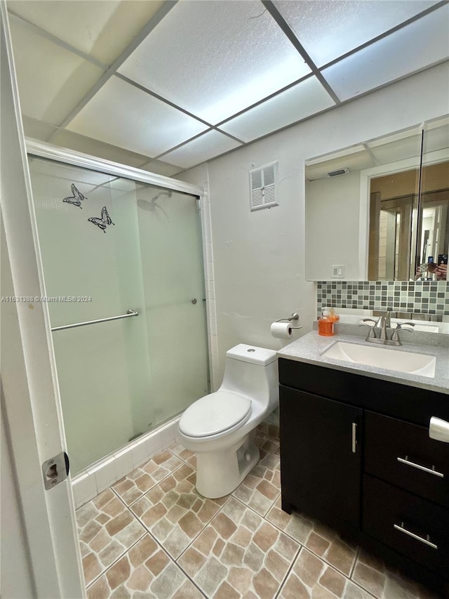 bathroom with tasteful backsplash, a paneled ceiling, toilet, vanity, and an enclosed shower