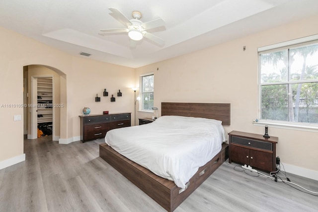 bedroom featuring light hardwood / wood-style floors, a raised ceiling, and ceiling fan