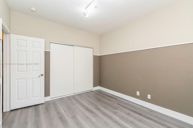 unfurnished bedroom featuring light hardwood / wood-style flooring, a closet, and track lighting