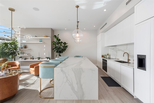 kitchen with pendant lighting, white cabinetry, sink, light stone counters, and light hardwood / wood-style floors