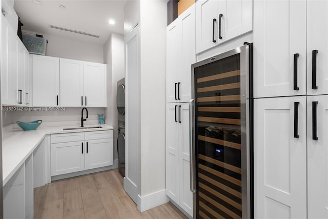 kitchen featuring white cabinetry, stacked washer / dryer, beverage cooler, and sink