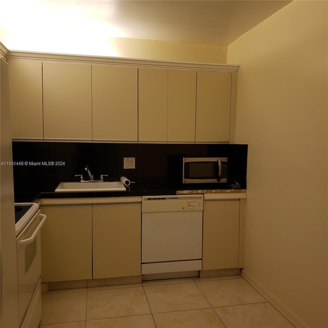 kitchen featuring white appliances, dark countertops, a sink, and light tile patterned flooring