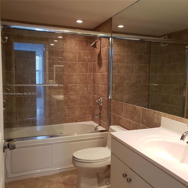 bathroom featuring toilet, shower / bath combination with glass door, tile walls, vanity, and tile patterned floors