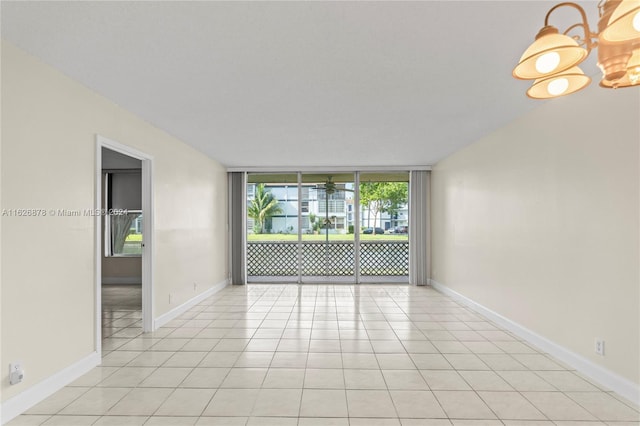 unfurnished room featuring an inviting chandelier, baseboards, light tile patterned floors, and a wall of windows