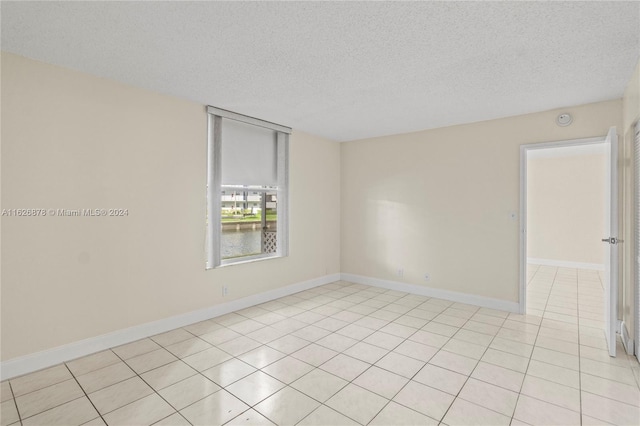 empty room featuring light tile patterned floors, baseboards, and a textured ceiling