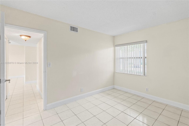 unfurnished room featuring visible vents, light tile patterned floors, a textured ceiling, and baseboards