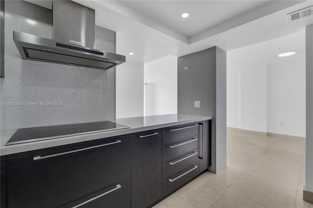 kitchen featuring wall chimney exhaust hood, backsplash, light tile patterned floors, and black electric stovetop