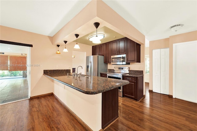 kitchen featuring decorative light fixtures, stainless steel appliances, kitchen peninsula, a kitchen breakfast bar, and dark wood-type flooring