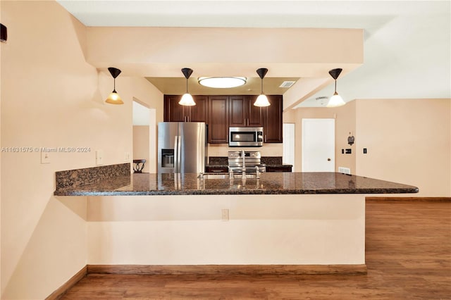 kitchen featuring kitchen peninsula, dark stone counters, stainless steel appliances, and decorative light fixtures