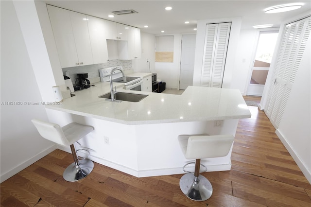 kitchen featuring kitchen peninsula, hardwood / wood-style floors, white cabinets, and a breakfast bar area