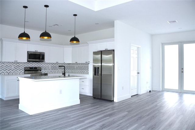 kitchen featuring decorative light fixtures, decorative backsplash, white cabinets, a center island with sink, and appliances with stainless steel finishes