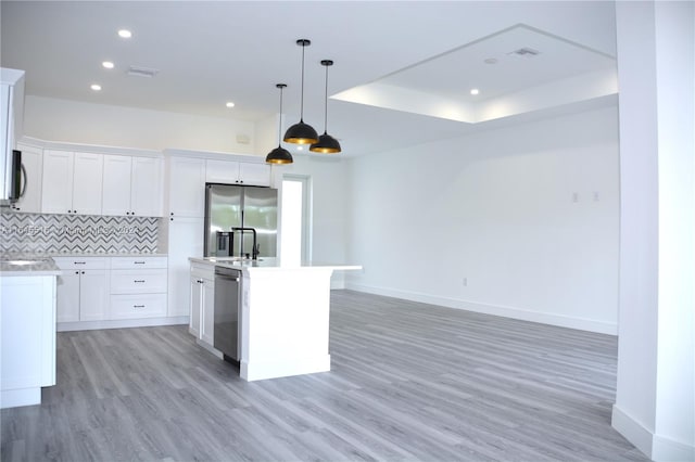 kitchen with appliances with stainless steel finishes, white cabinets, decorative backsplash, a kitchen island with sink, and light wood-type flooring