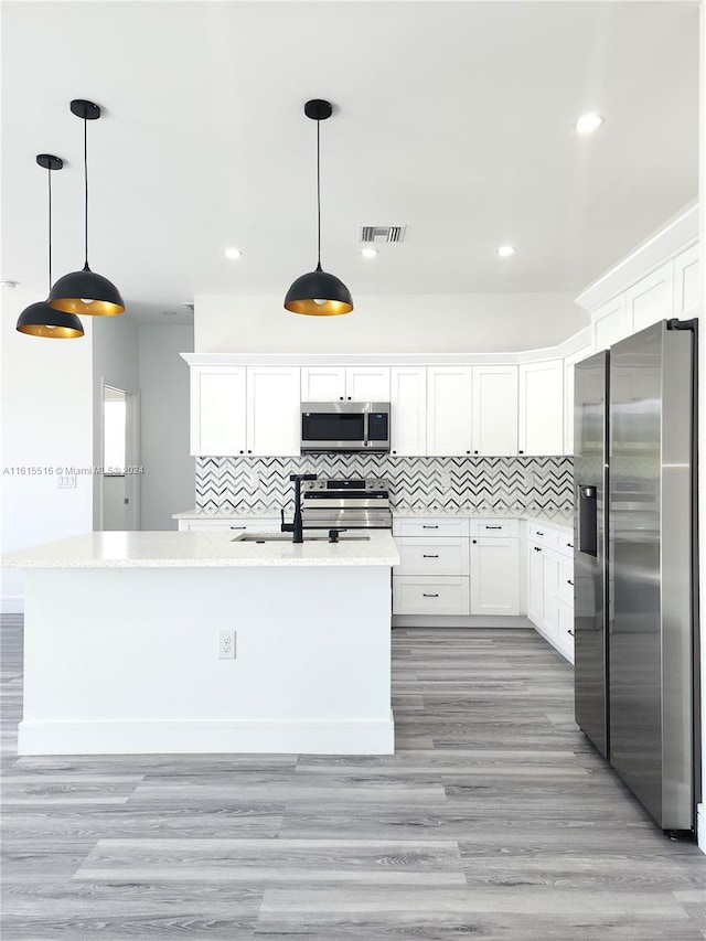 kitchen featuring appliances with stainless steel finishes, light wood-type flooring, tasteful backsplash, and an island with sink