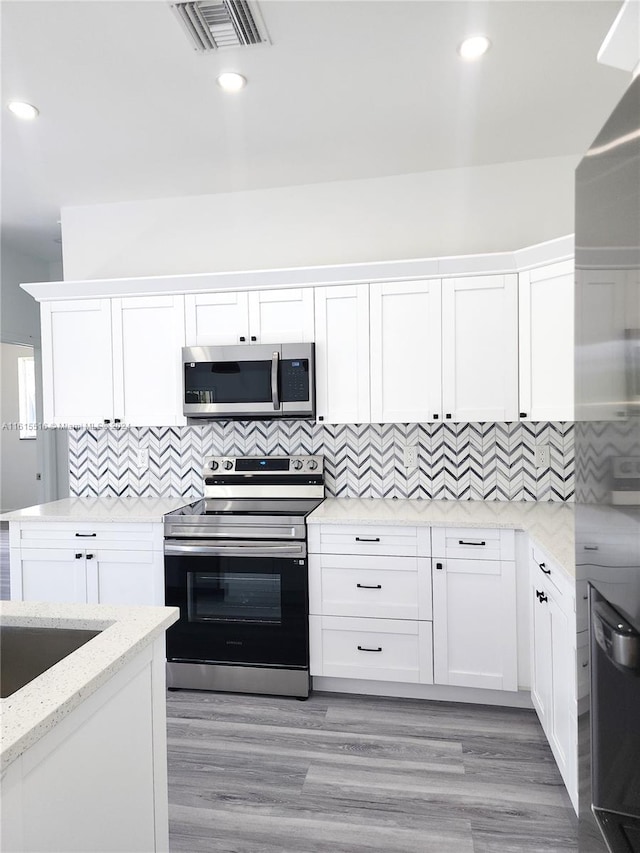 kitchen with white cabinetry, stainless steel appliances, light hardwood / wood-style floors, and backsplash