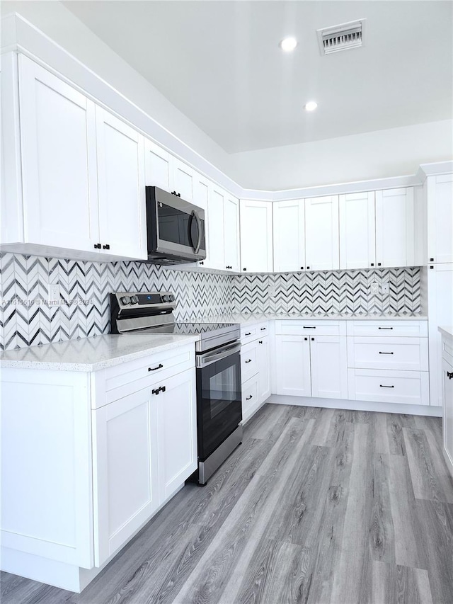 kitchen with light hardwood / wood-style flooring, tasteful backsplash, stainless steel appliances, and white cabinetry