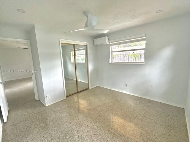 unfurnished bedroom featuring a wall mounted air conditioner, a textured ceiling, ceiling fan, and a closet