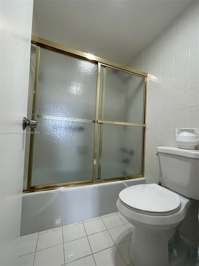 bathroom featuring tile walls, bath / shower combo with glass door, tile patterned floors, and toilet