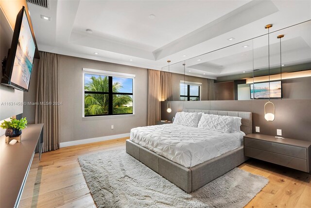 bedroom with light hardwood / wood-style floors and a tray ceiling