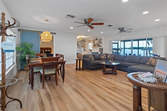 living room featuring a barn door, ceiling fan, a water view, and light hardwood / wood-style floors