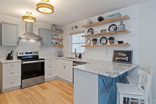 kitchen with wall chimney range hood, sink, appliances with stainless steel finishes, light hardwood / wood-style floors, and light stone counters