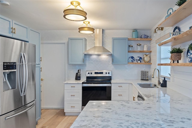 kitchen with light stone counters, wall chimney exhaust hood, stainless steel appliances, sink, and light hardwood / wood-style flooring