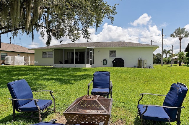 back of property featuring a sunroom, a yard, and an outdoor fire pit