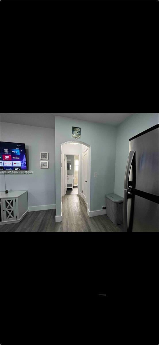 hallway featuring arched walkways, wood finished floors, and baseboards