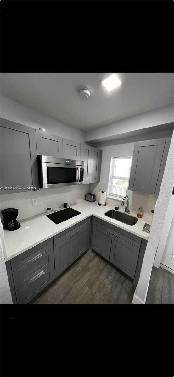 kitchen featuring black electric cooktop, a sink, light countertops, gray cabinets, and stainless steel microwave