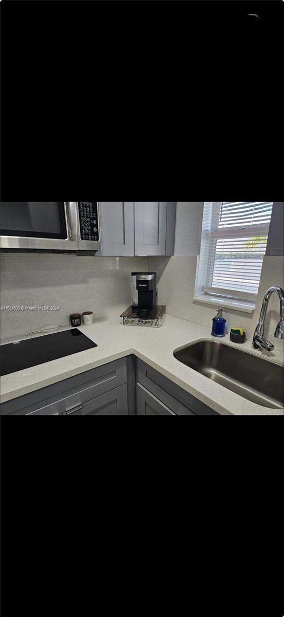 kitchen with light countertops, stainless steel microwave, a sink, and gray cabinetry