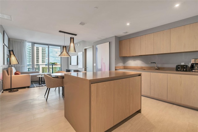 kitchen with pendant lighting, light brown cabinets, sink, a kitchen island, and light hardwood / wood-style flooring