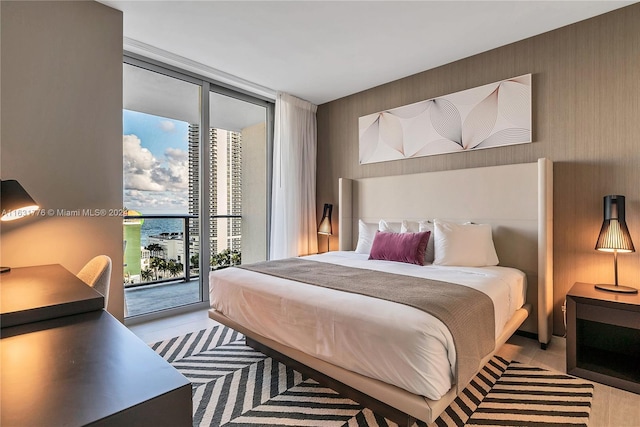 bedroom with light hardwood / wood-style flooring, a water view, expansive windows, and access to outside