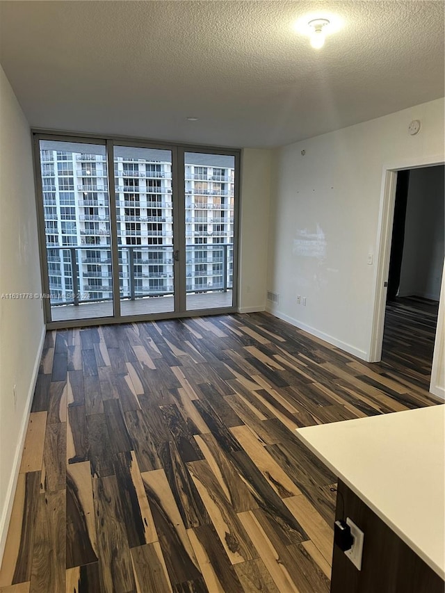 unfurnished room with dark wood-type flooring, a textured ceiling, and floor to ceiling windows