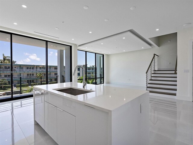 kitchen with floor to ceiling windows, sink, a kitchen island with sink, and white cabinets