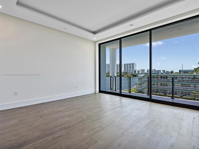 unfurnished room with wood-type flooring, a tray ceiling, and floor to ceiling windows