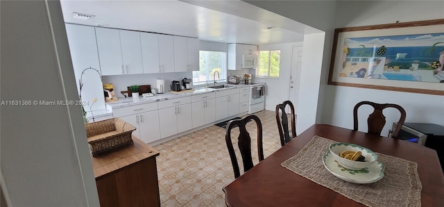 interior space featuring electric range, sink, white cabinetry, and light tile patterned floors