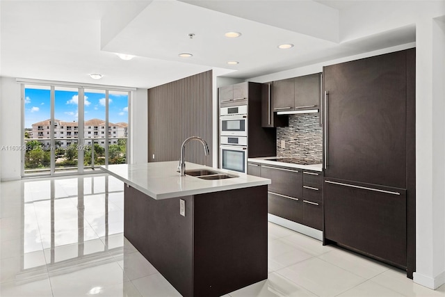 kitchen with sink, backsplash, light tile patterned floors, an island with sink, and double oven