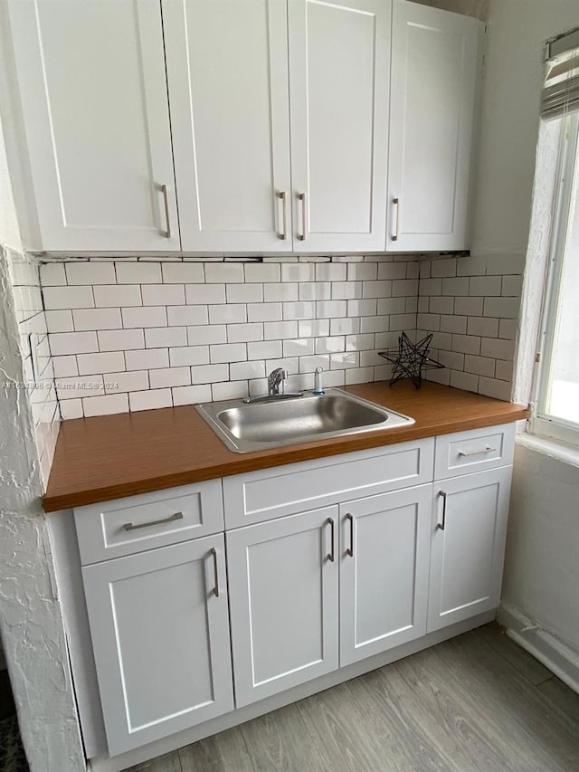 kitchen with wood counters, sink, white cabinetry, light hardwood / wood-style flooring, and decorative backsplash