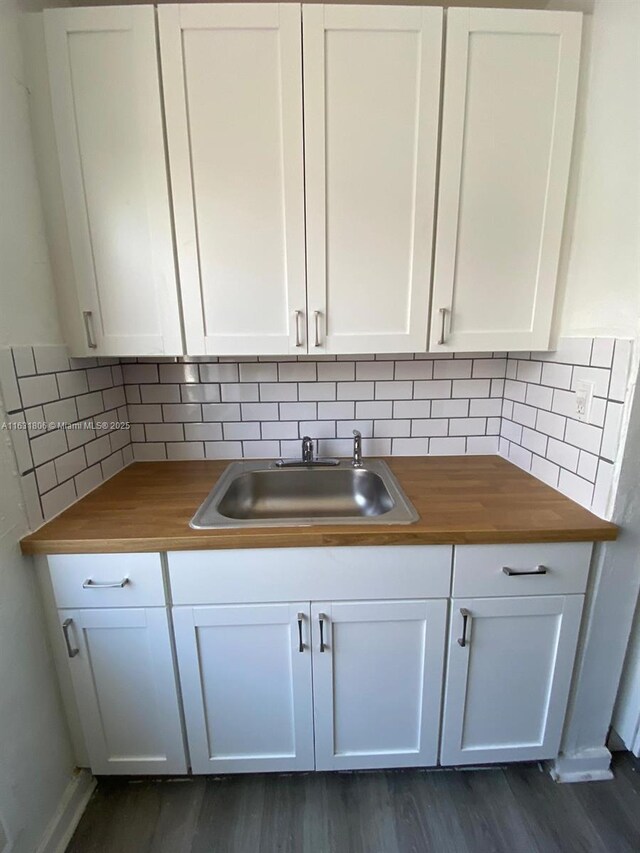 interior details featuring wood counters, tasteful backsplash, sink, white cabinets, and dark wood-type flooring