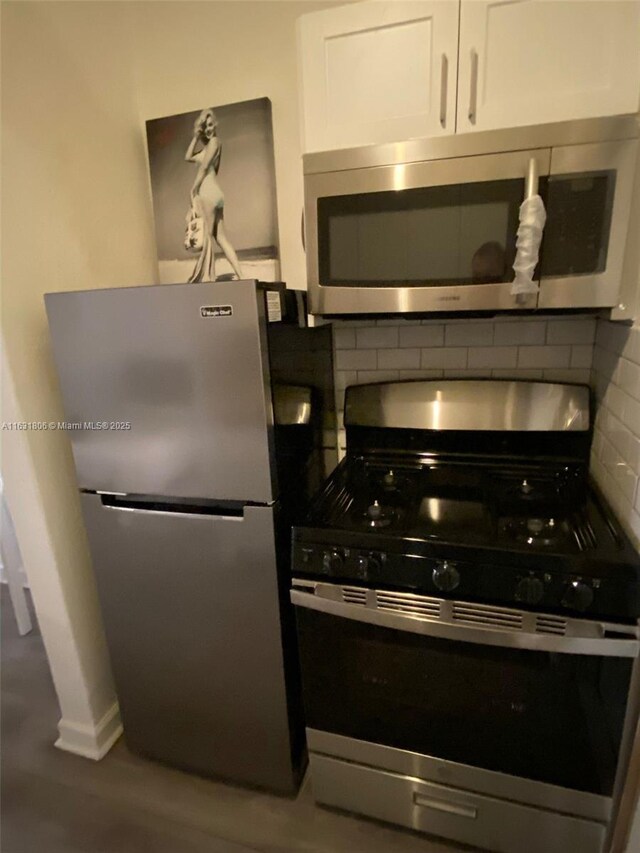 kitchen with tasteful backsplash, hardwood / wood-style flooring, white cabinets, and appliances with stainless steel finishes