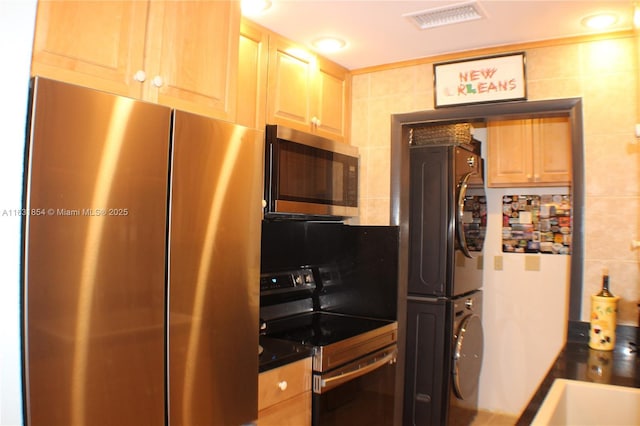 kitchen featuring stacked washer and clothes dryer, tile walls, light brown cabinetry, tasteful backsplash, and appliances with stainless steel finishes