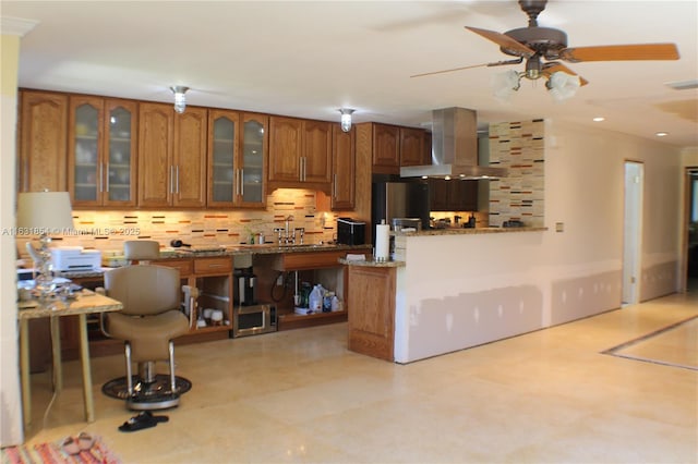 kitchen featuring light stone countertops, kitchen peninsula, tasteful backsplash, exhaust hood, and a breakfast bar area