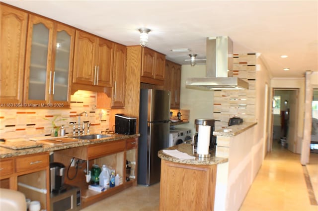 kitchen featuring light stone countertops, stainless steel fridge, island range hood, and sink