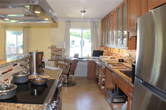 kitchen with light stone countertops, stainless steel fridge, backsplash, stove, and ventilation hood