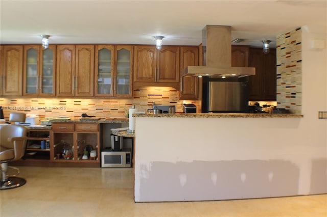 kitchen featuring light stone counters, backsplash, extractor fan, and fridge