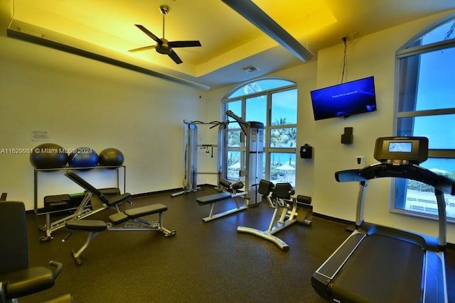 workout area featuring ceiling fan, a tray ceiling, and a healthy amount of sunlight