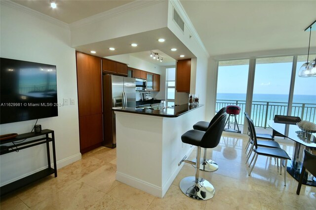 kitchen featuring decorative light fixtures, a water view, ornamental molding, appliances with stainless steel finishes, and light tile patterned floors