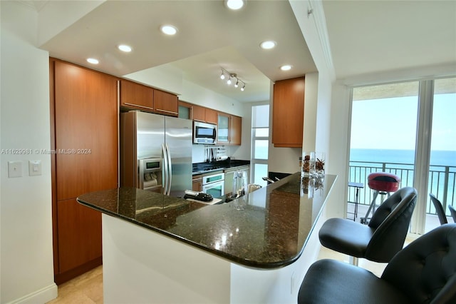 kitchen with a kitchen bar, appliances with stainless steel finishes, track lighting, kitchen peninsula, and a water view