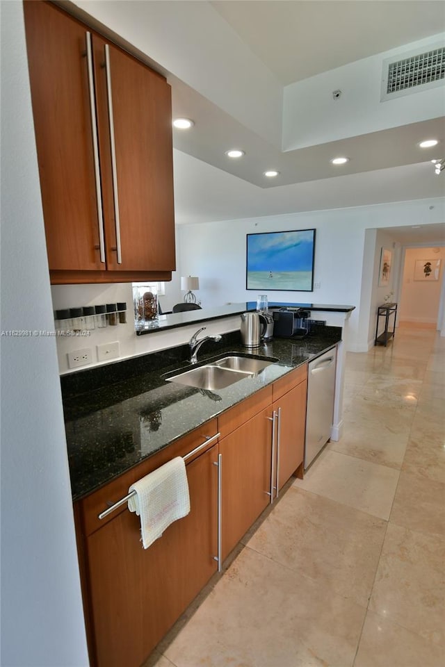 kitchen with stainless steel dishwasher, dark stone counters, and sink