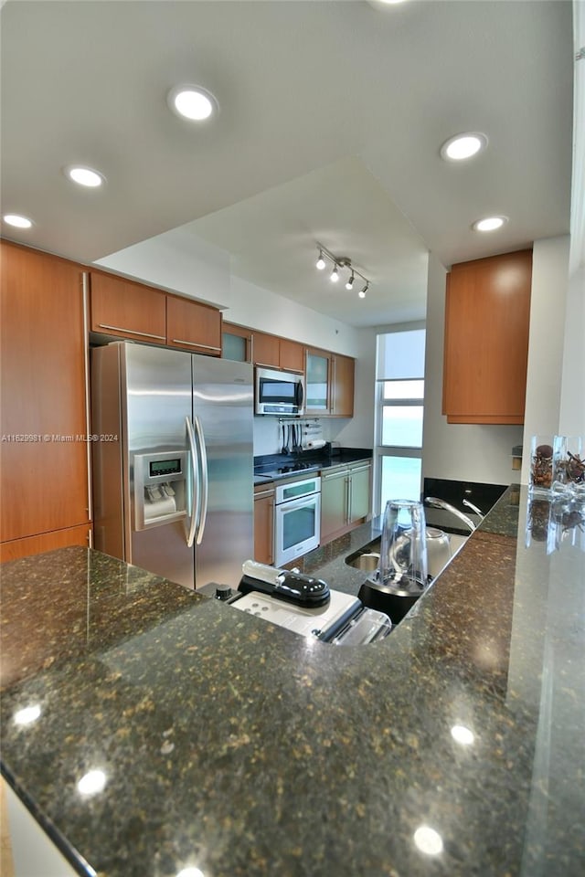 kitchen with dark stone counters, track lighting, and appliances with stainless steel finishes