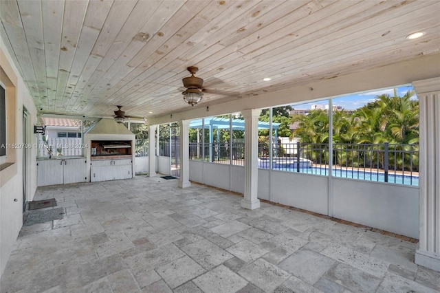 unfurnished sunroom featuring wooden ceiling, ceiling fan, and ornate columns